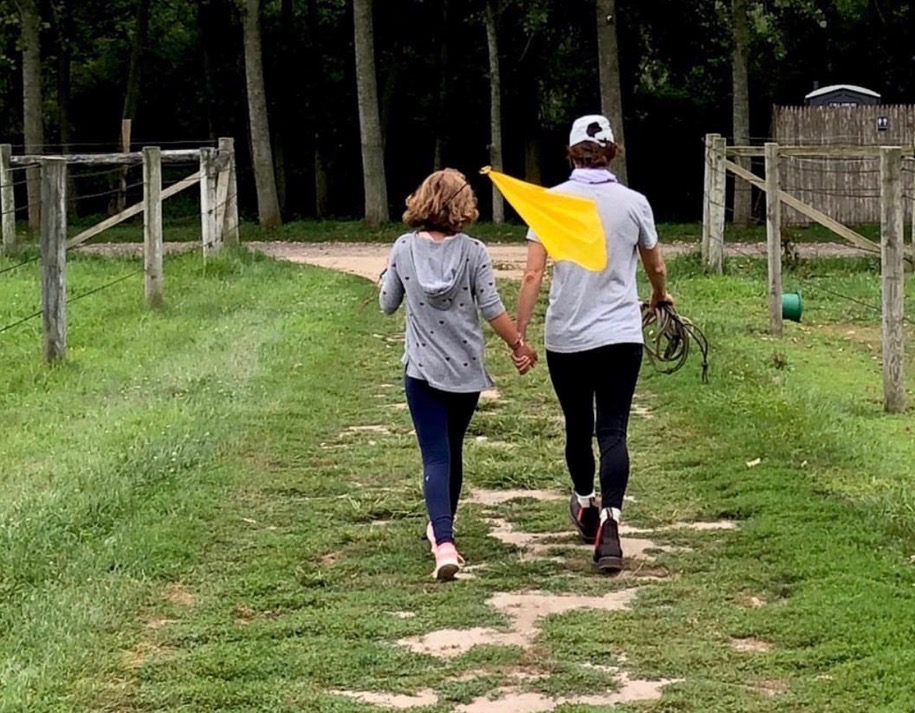 Two people walking hand-in-hand along a grassy path toward a wooded area