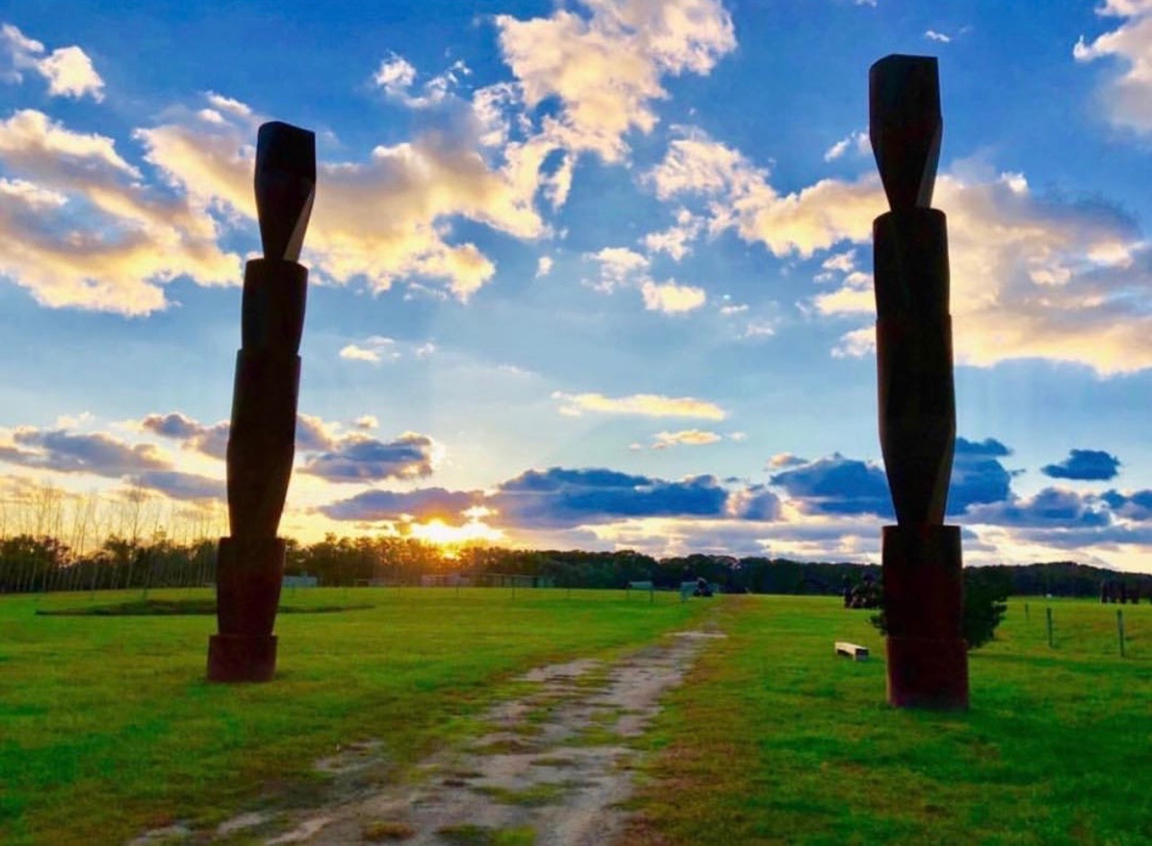 Two tall modern sculptures flanking a path through an open field at sunset
